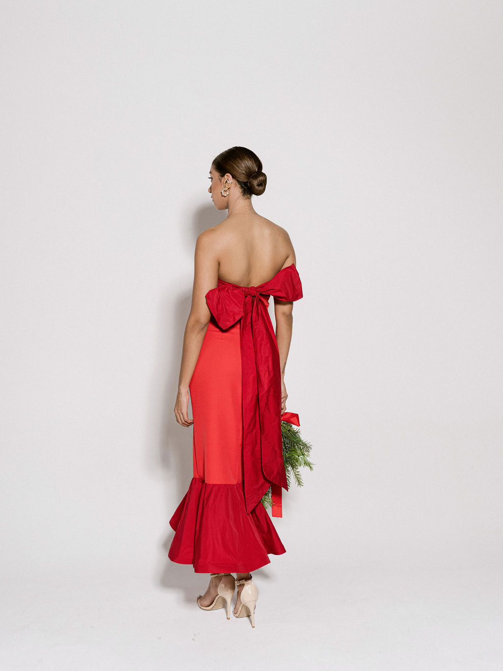 A model wearing a red dress with a ruffled hem and a bow on the back by Monica Arguedas.