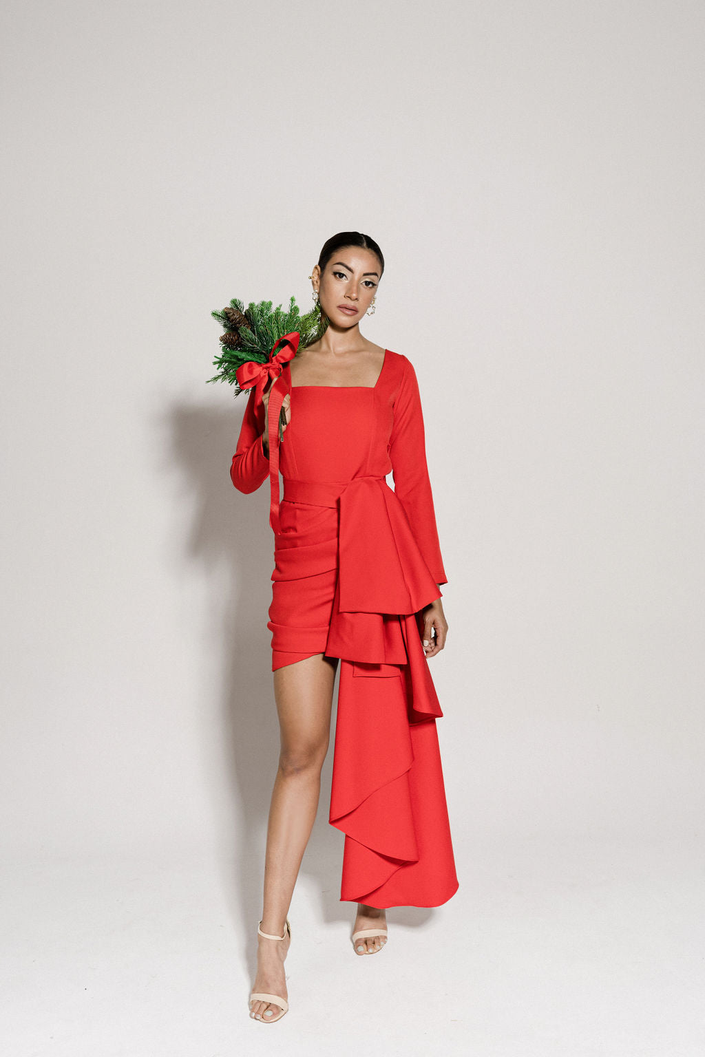 A model wearing a red dress with long sleeves and a draped panel by Monica Arguedas