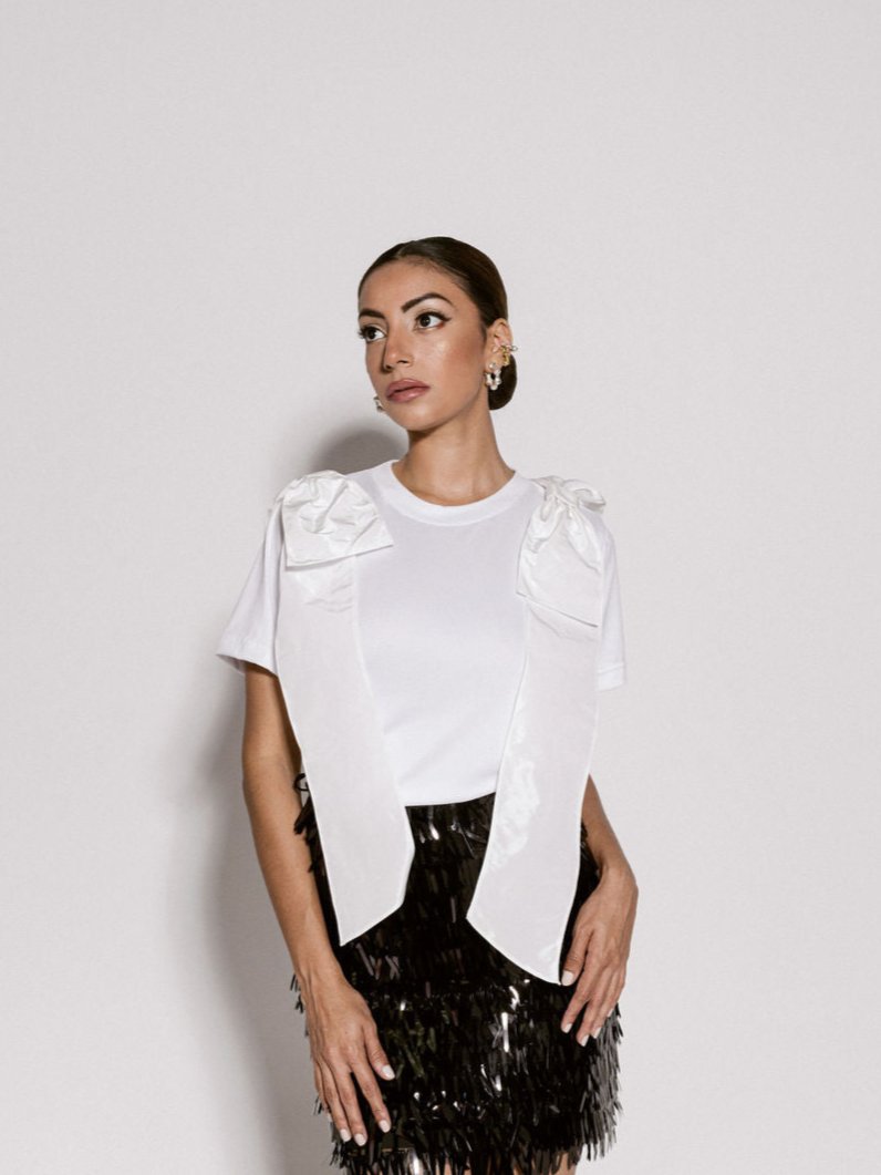 A model wearing a white top with bows on the shoulder by Monica Arguedas.
