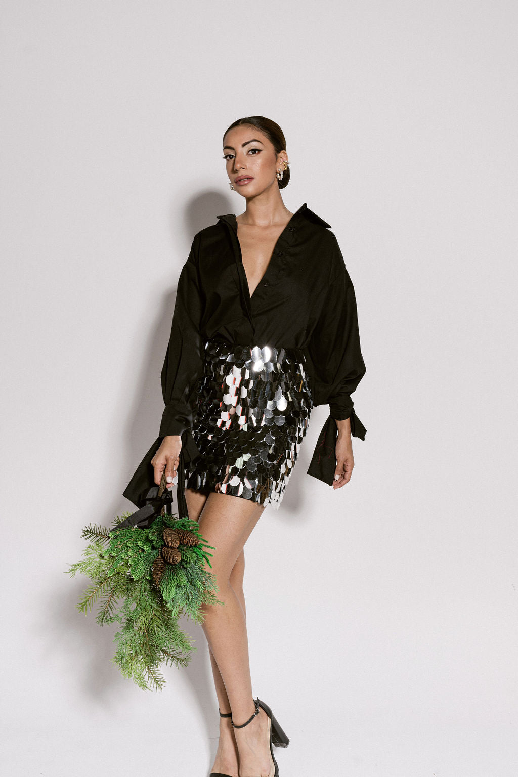 A model wearing a black top with puffy sleeves and bows on the cuffs paired with a silver sequin skirt by Monica Arguedas.