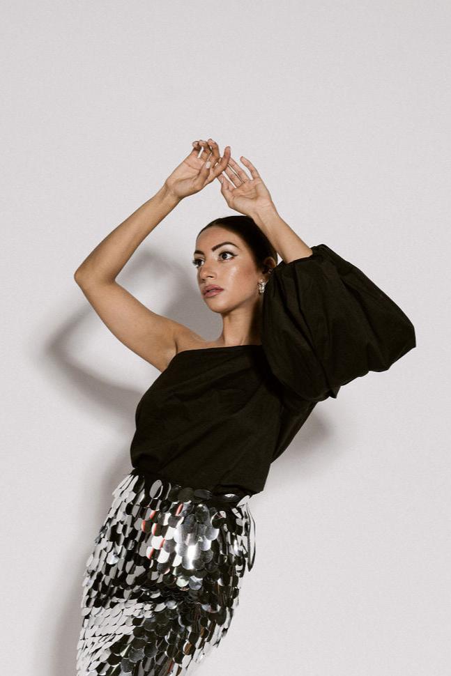 A model wearing a one shoulder black top with a puffy sleeve by Monica Arguedas.