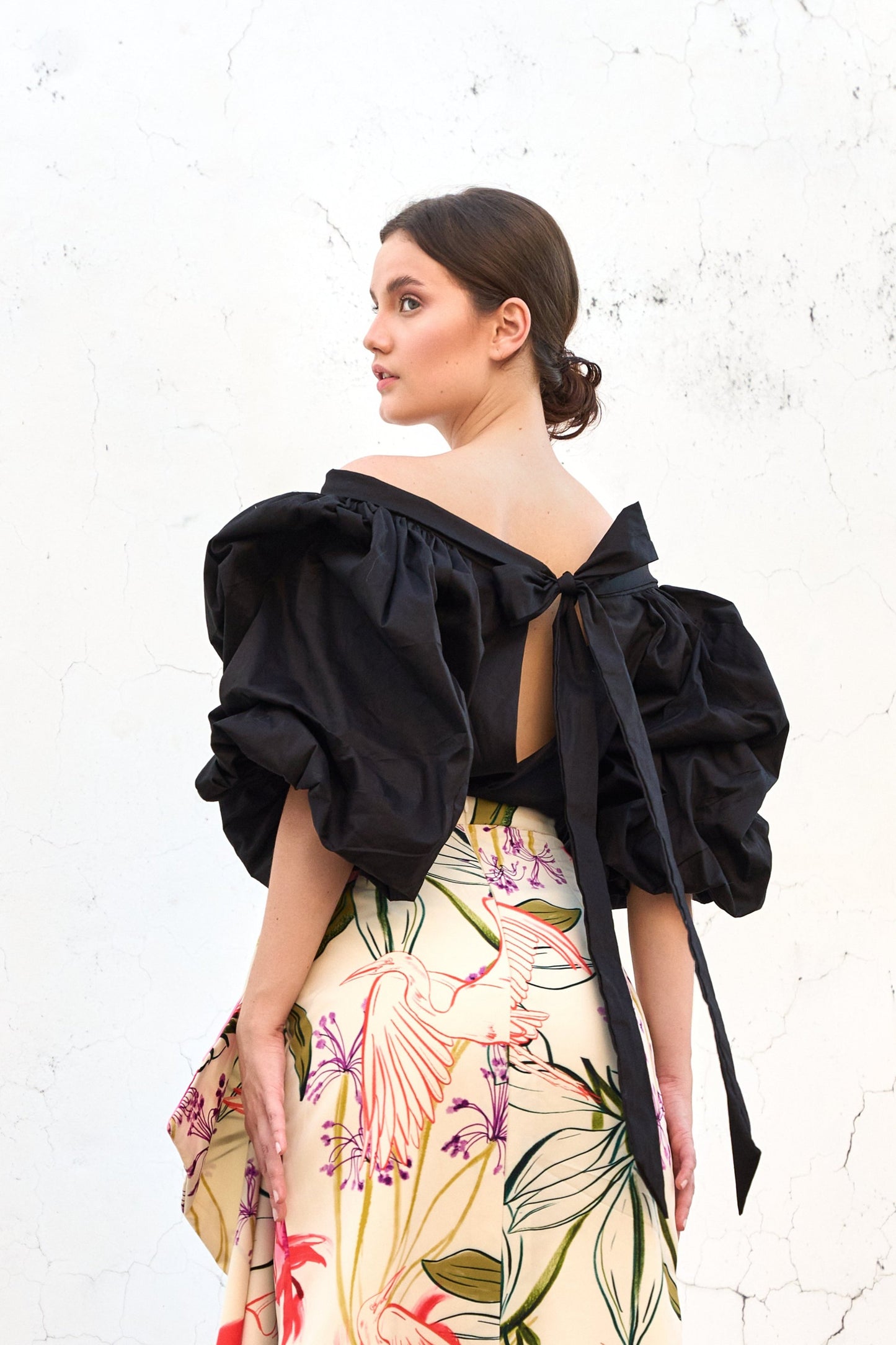 A model wearing a black top with puffy sleeves and a bow detail on the back by Monica Arguedas.