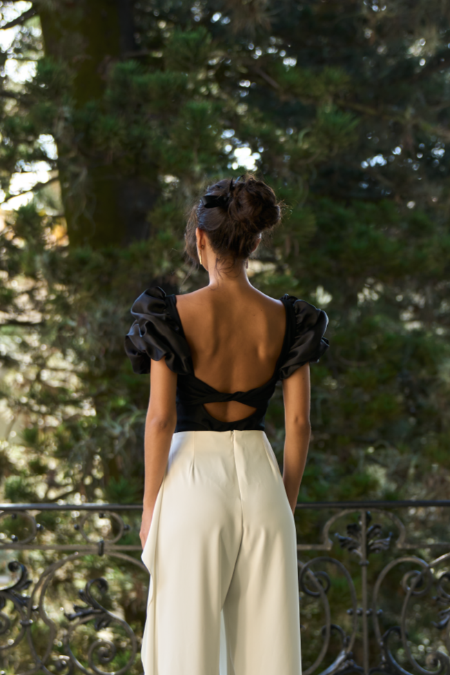 A model wearing a Black bodysuit with puffy sleves and an open twisted back by Monica Arguedas.