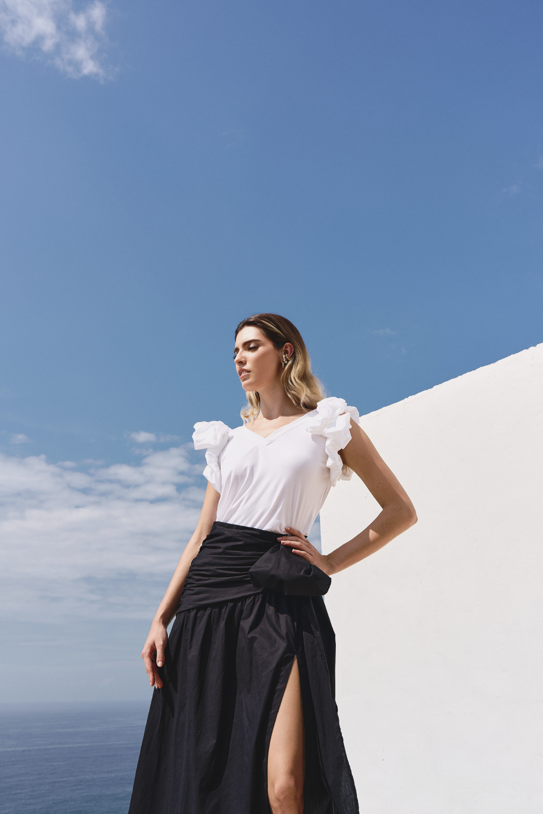 A model wearing a solid black skirt with a bow and slit by Monica Arguedas