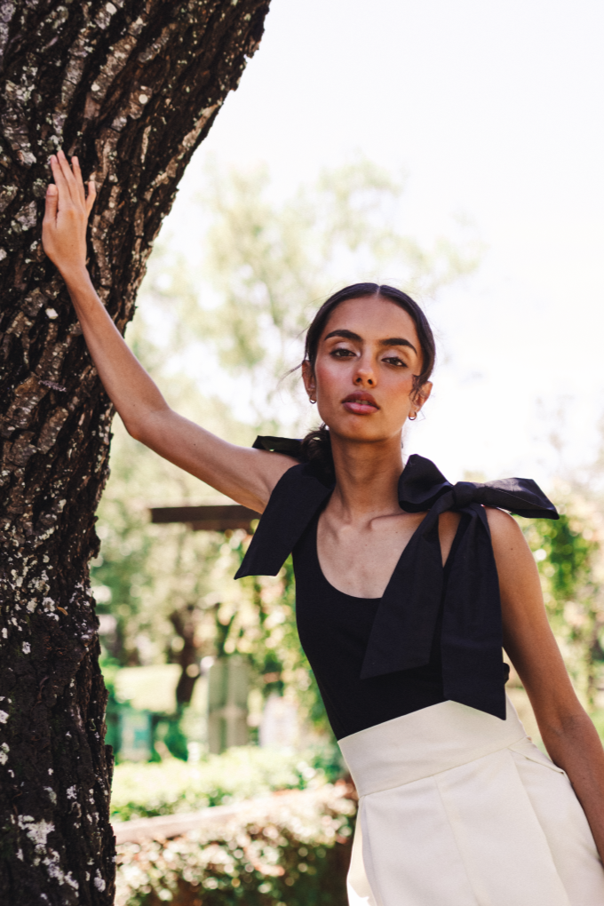 Model wearing a top solid black with bows on the shoulders in a salvadoran forest.