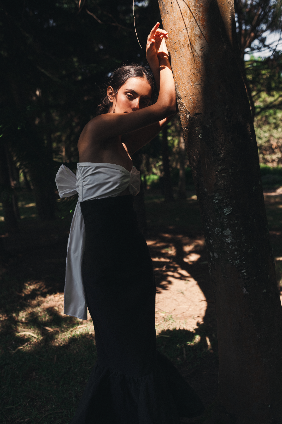 Model wearing a sleveeless black and white dress with a decorative bow in the back in a salvadoran forest.