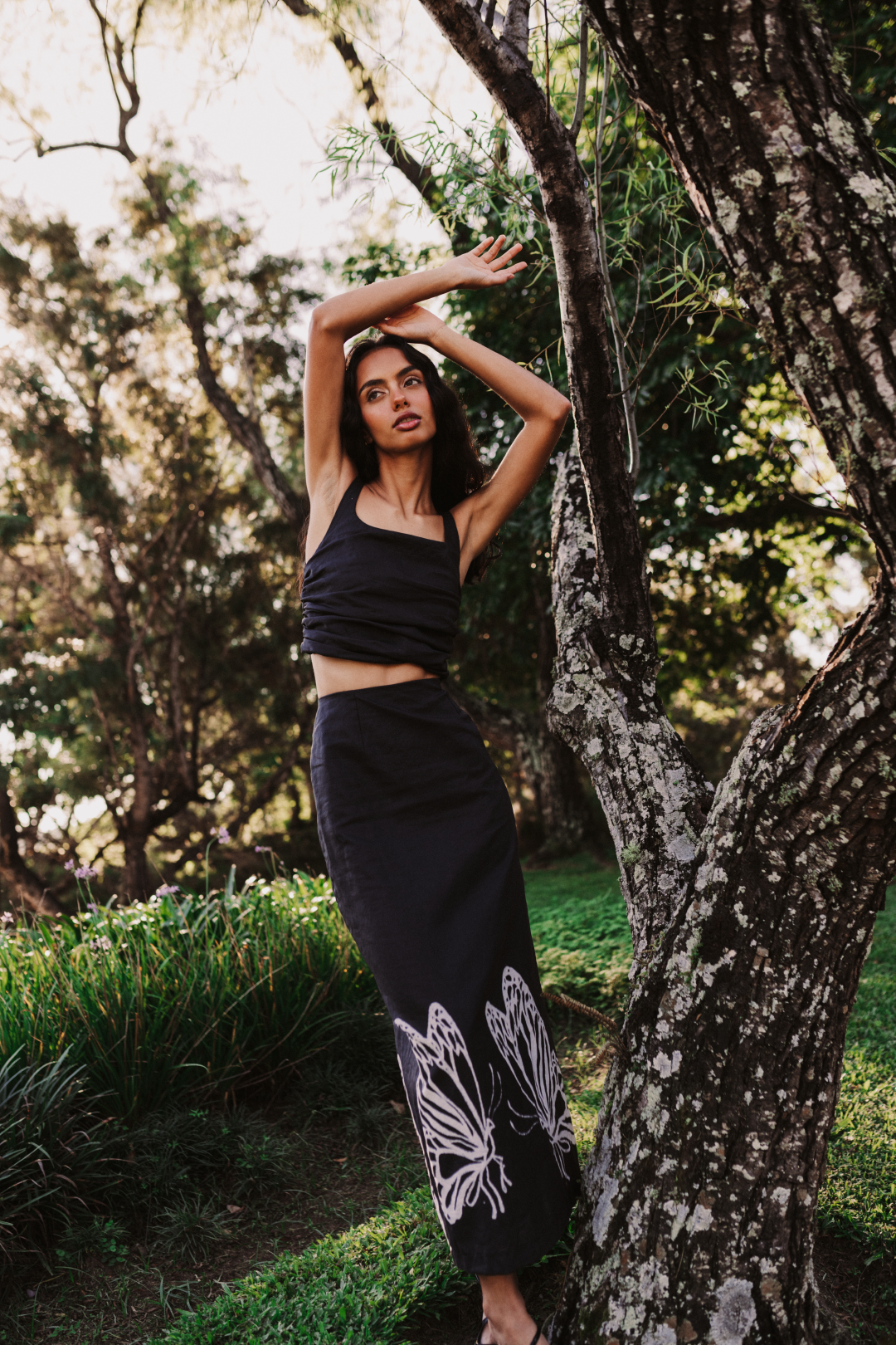 A model wearing a black top with an open twisted back paired with a long black skirt with a white butterfly print by Monica Arguedas.