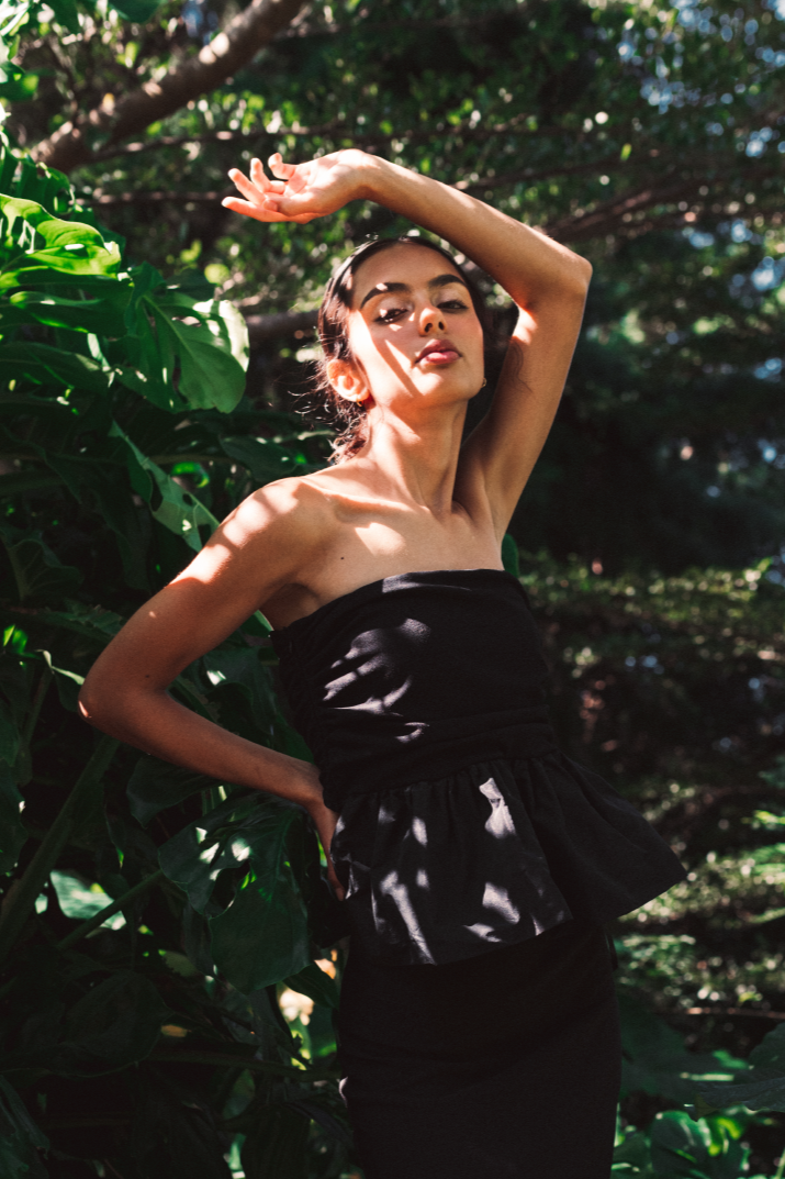 Model wearing a set with a sleeveless black top and a midi solid black skirt with stirs surrounded by a salvadoran forest.