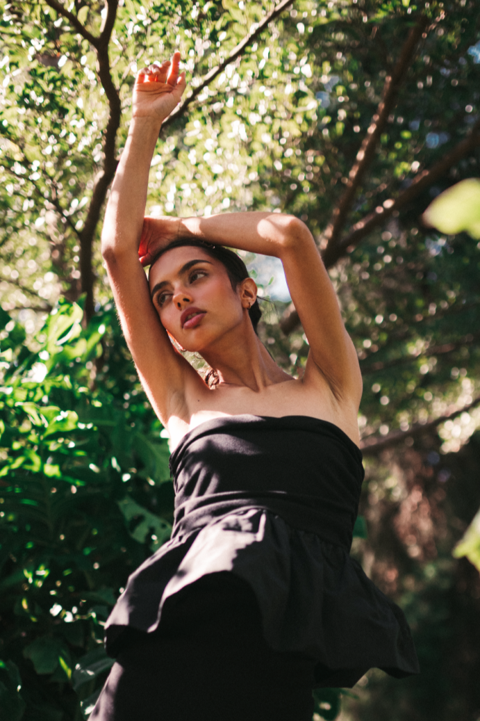 Model wearing a set with a sleeveless black top and a midi solid black skirt with stirs surrounded by a salvadoran forest.