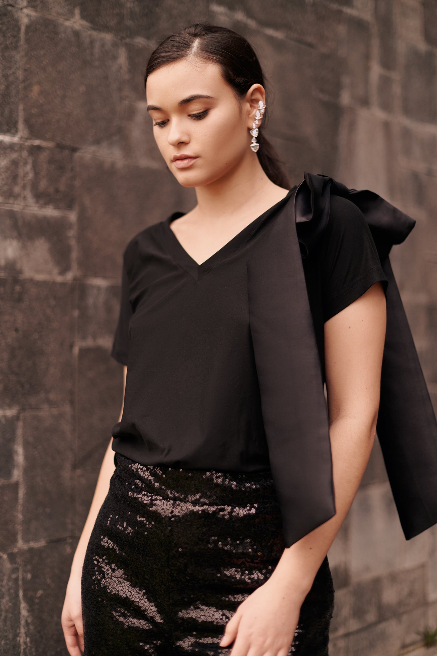 A model wearing a solid black top with a bow on the shoulder by Monica Arguedas.