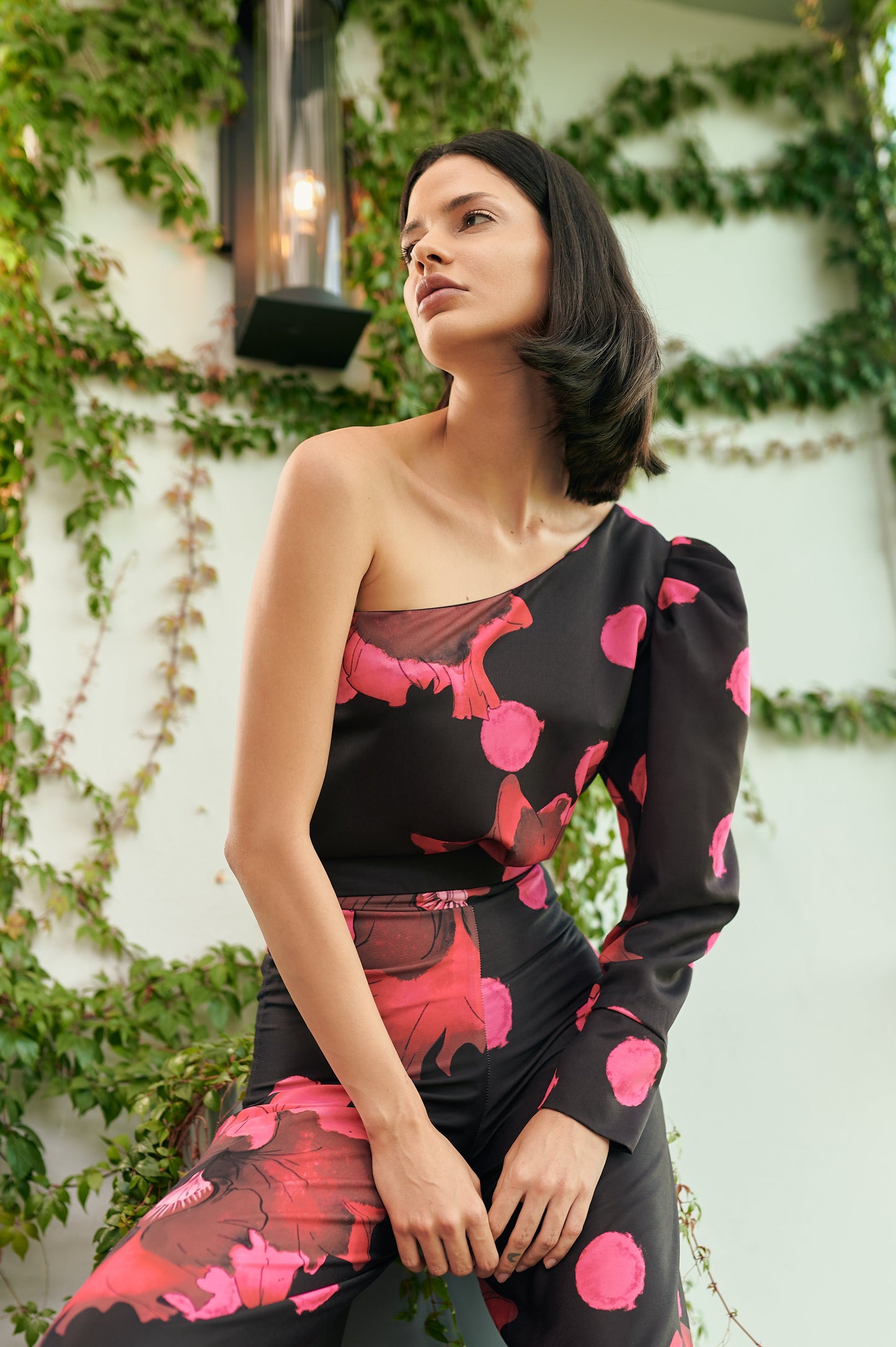 A model wearing a black one shoulder top with a puffy sleeve and pink dotted flower print by Monica Arguedas.