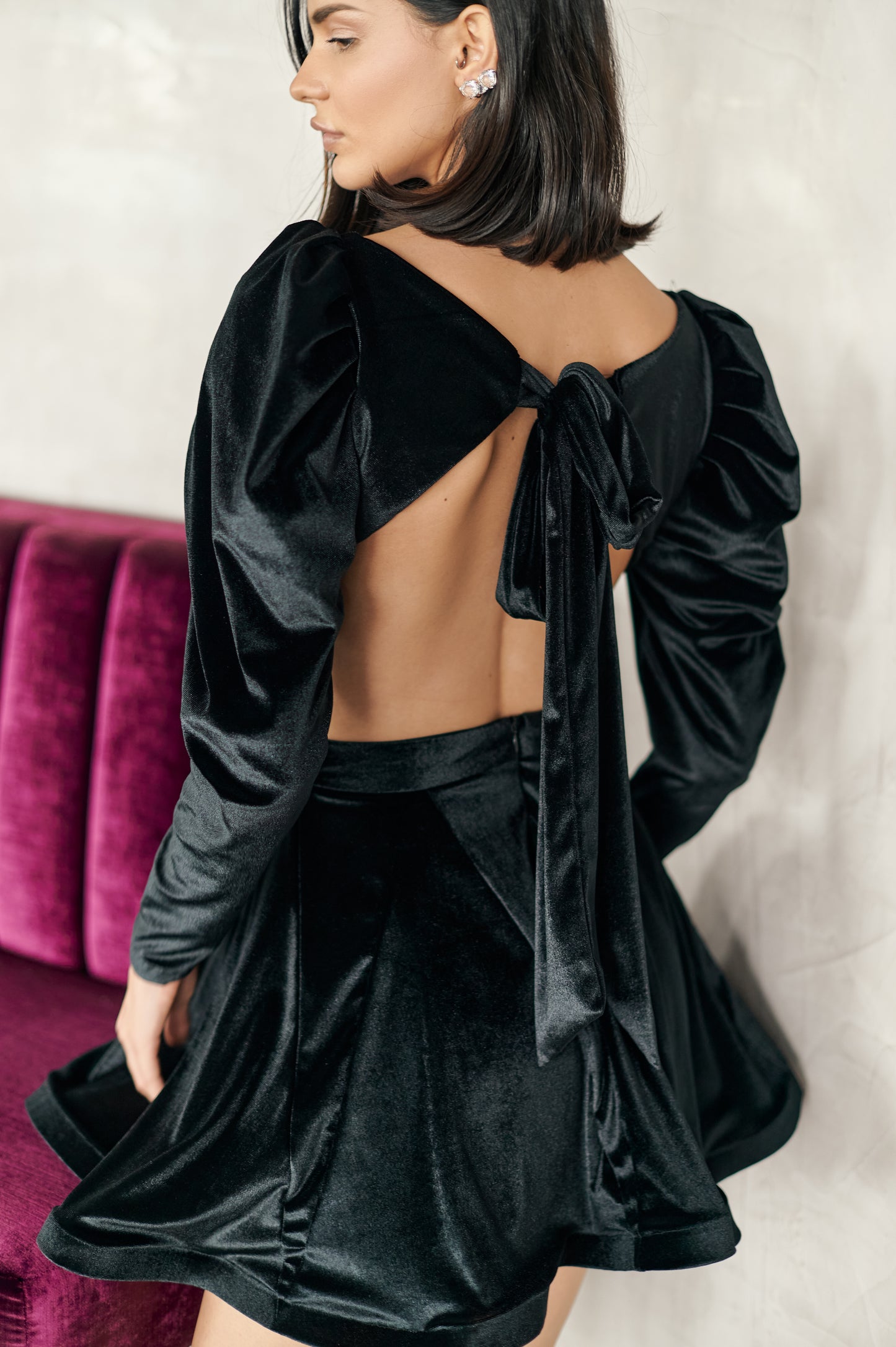 A model wearing a black dress with puffy sleeves, cut outs on the sides, and an open back by Monica Arguedas.