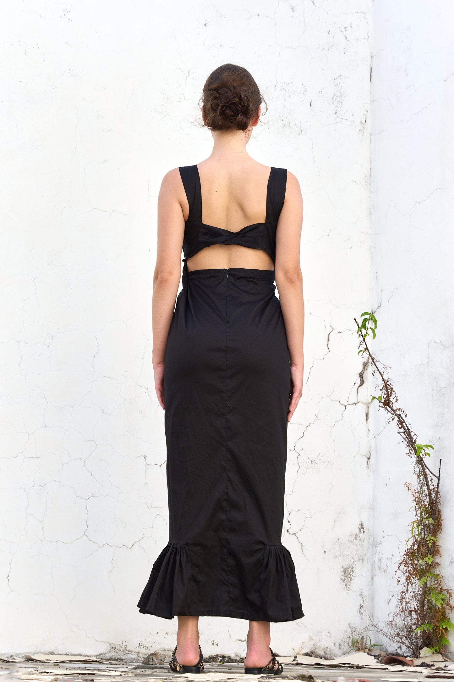 A model wearing a black dress with a deep v-neck and a ruffled hem by Monica Arguedas.