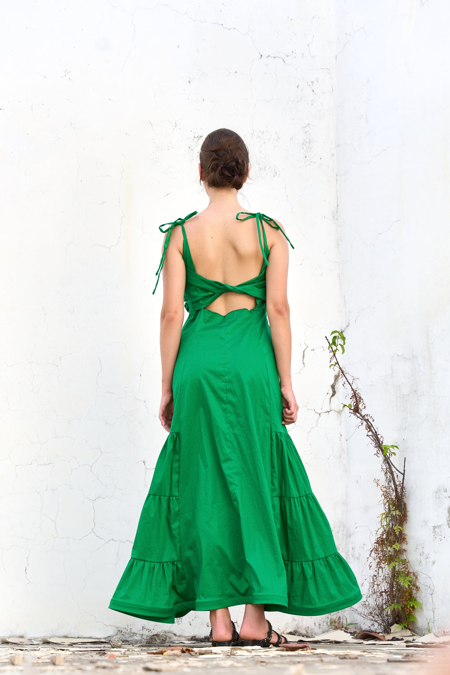 A model wearing a green dress with ruffled panels and a twisted detail on the back by Monica Arguedas.