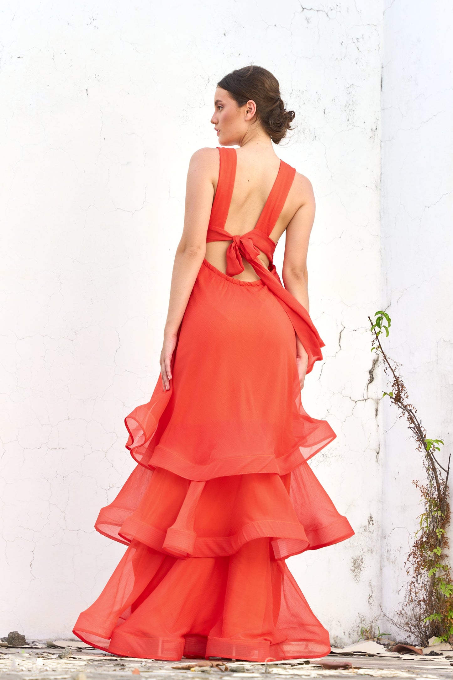 A model wearing a red dress with ruffled panels by Monica Arguedas.
