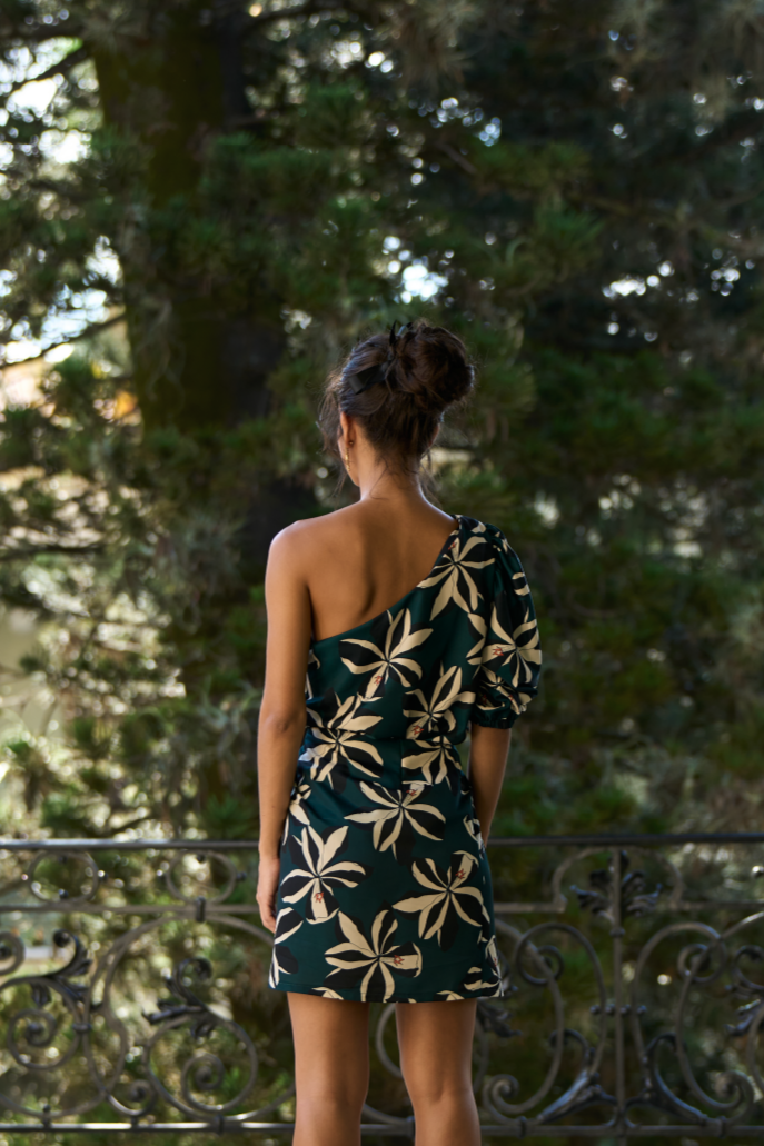 A model wearing an aqua one shoulder top with creme and black flower print and a puffy sleeve by Monica Arguedas.