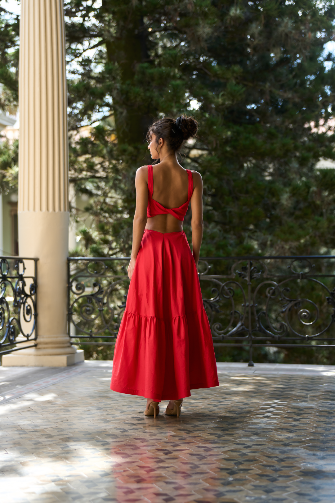 A model wearing a red dress with a bow on the front and a twisted back detail by Monica Arguedas.