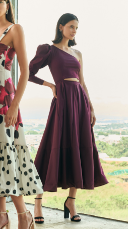 A model wearing a one shoulder burgundy dress with a puffy sleeve by Monica Arguedas.