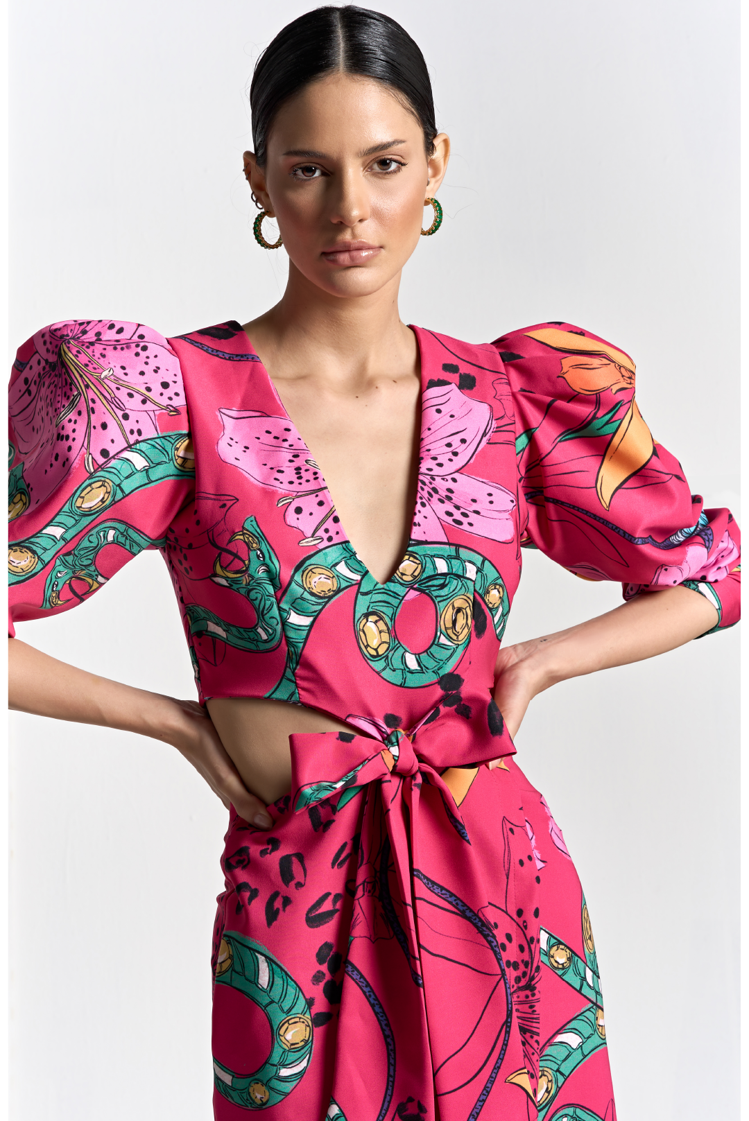A model wearing a bright pink floral print dress with cuts on the sides and bow in the middle by Monica Arguedas.