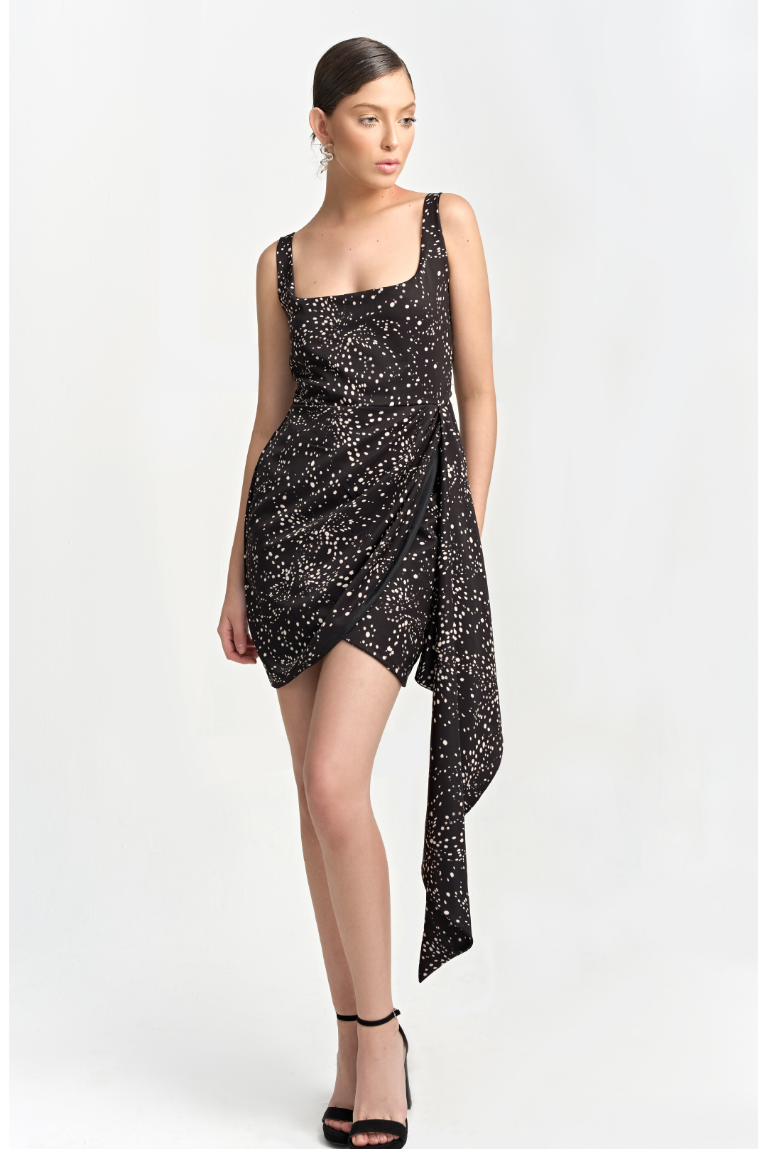 A model wearing a black mini dress with creme dots and a draped panel on the side by Monica Arguedas.