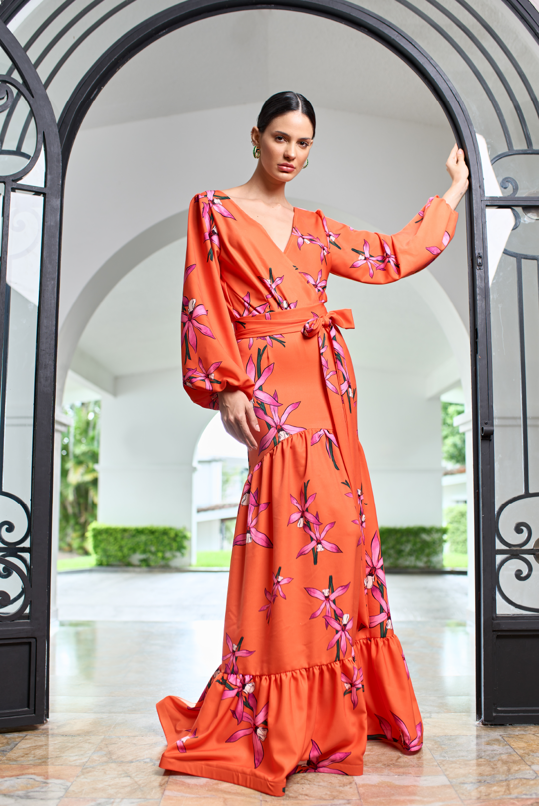 Model wearing a long drapped orange skirt with a bow around the waist with a pink flower print by Monica Arguedas.