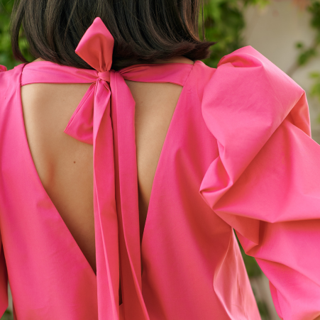 A model wearing a bright pink dress with puffy sleeves and an open back by Monica Arguedas.