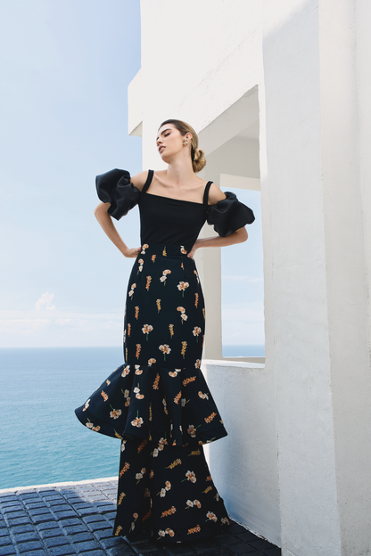 A model wearing a black ruffled skirt with floral print by Monica Arguedas