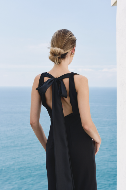 A model wearing a solid black dress with an open back and a bow in the back of the shoulders by Monica Arguedas.