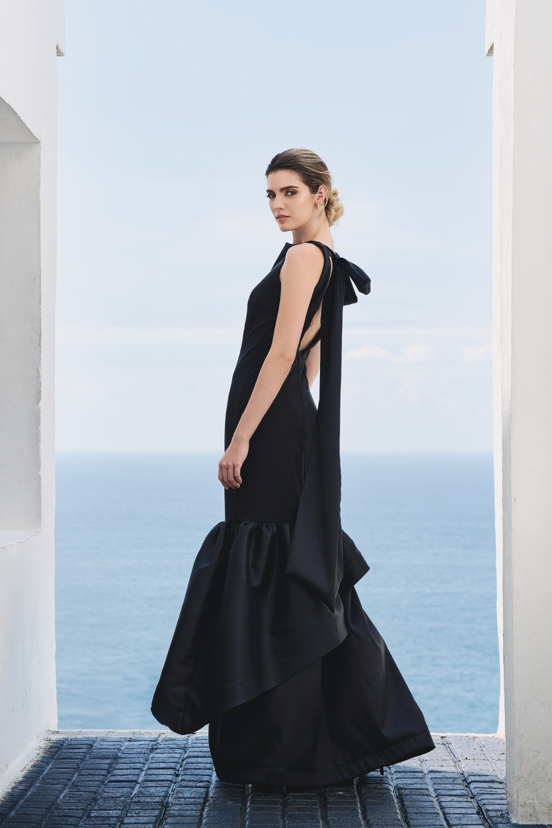 A model wearing a solid black dress with ruffles by Monica Arguedas.
