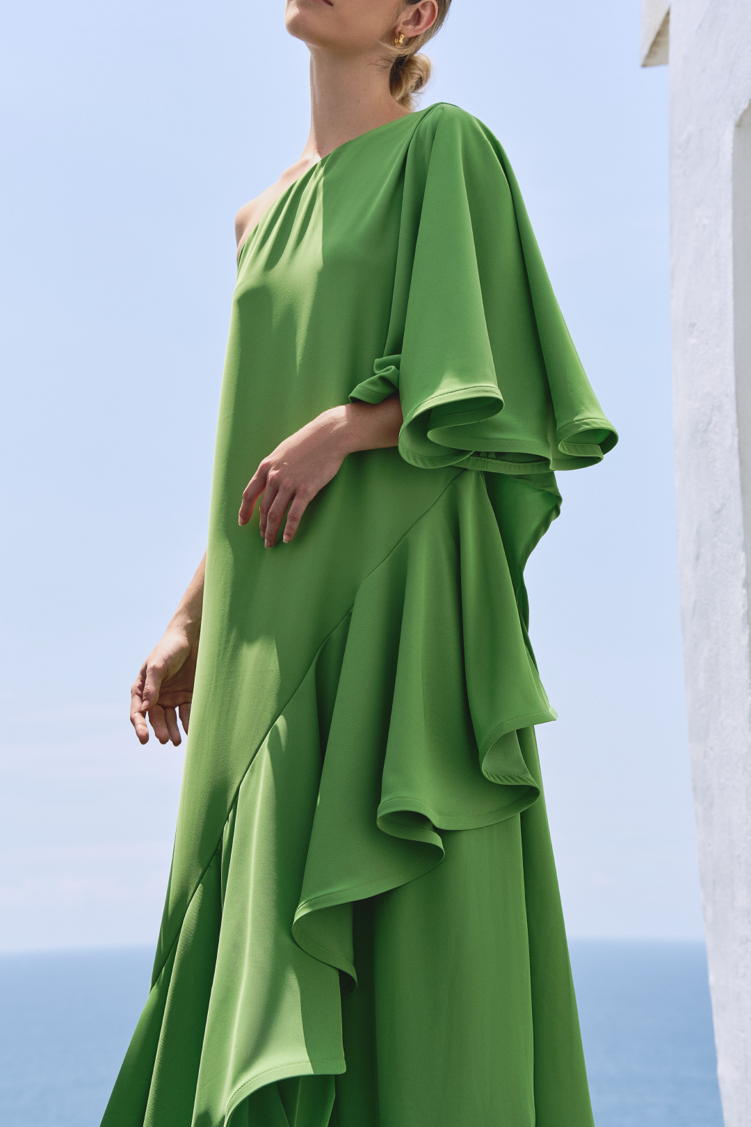 A model wearing a solid green one shoulder flowy top by Monica Arguedas.