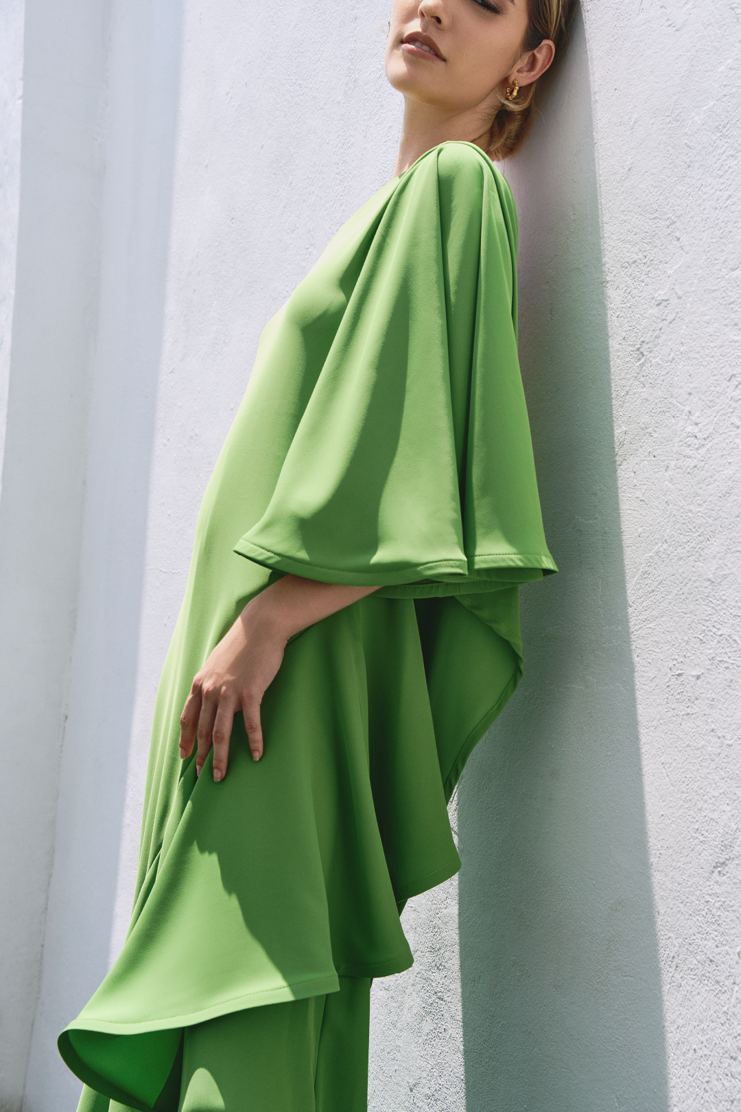 A model wearing a solid green one shoulder flowy top by Monica Arguedas.