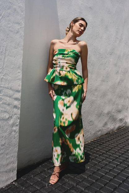 A model wearing a green ruffled tube top and flowy skirt with blurred floral print by Monica Arguedas