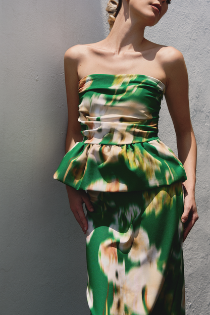 A model wearing a green ruffled tube top and flowy skirt with blurred floral print by Monica Arguedas