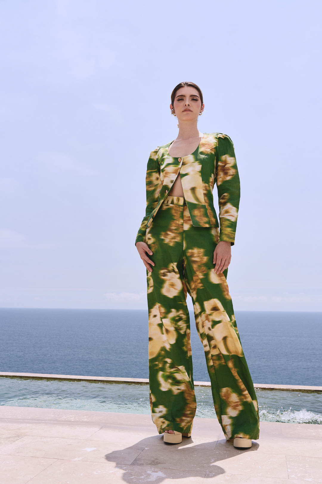 A model wearing green long-sleeved buttoned top and pants with a blurred floral print by Monica Arguedas