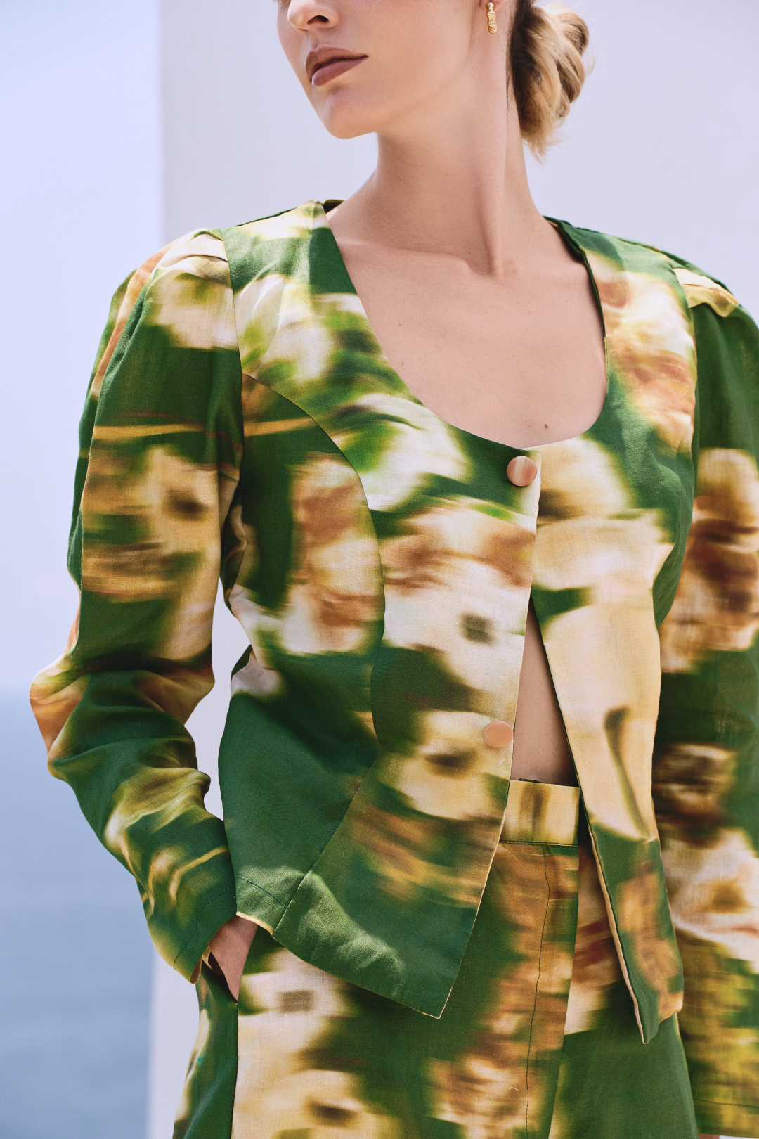 A model wearing green long-sleeved buttoned top with a blurred floral print by Monica Arguedas