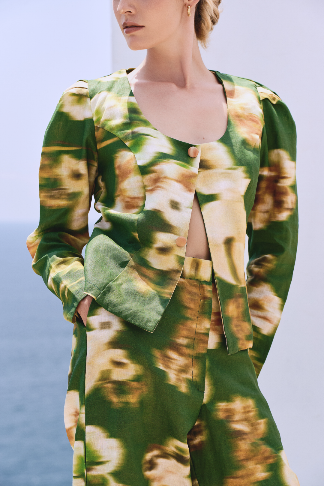 A model wearing green long-sleeved buttoned top and pants with a blurred floral print by Monica Arguedas