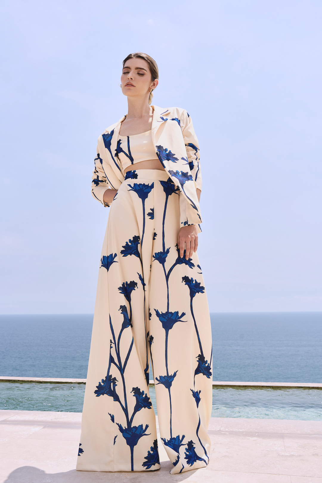 A model wearing a cream blazer and flowy pants with blue flowers by Monica Arguedas