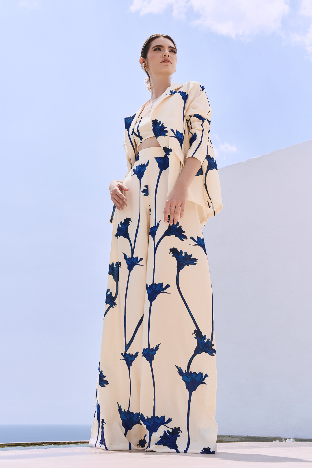 A model wearing a cream blazer and flowy pants with blue flowers by Monica Arguedas
