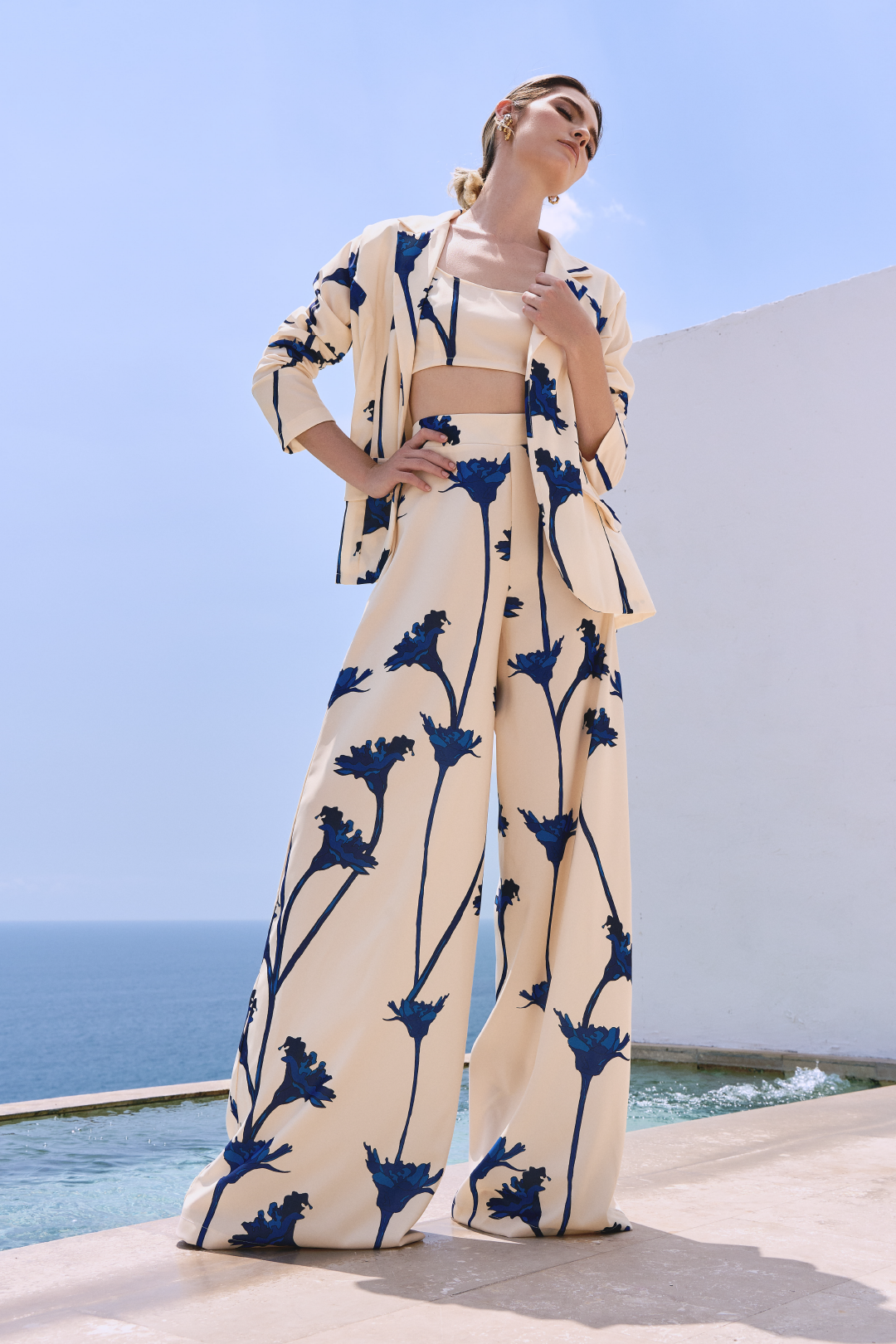 A model wearing a cream blazer and flowy pants with blue flowers by Monica Arguedas