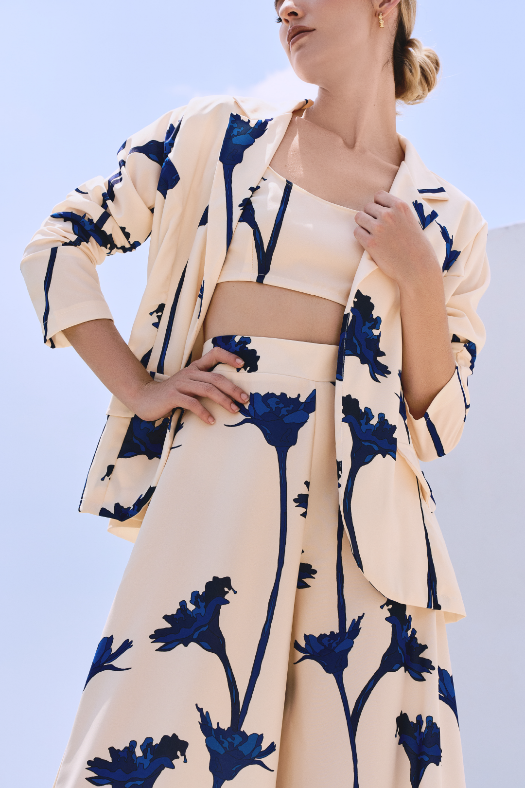 A model wearing a cream blazer and flowy pants with blue flowers by Monica Arguedas