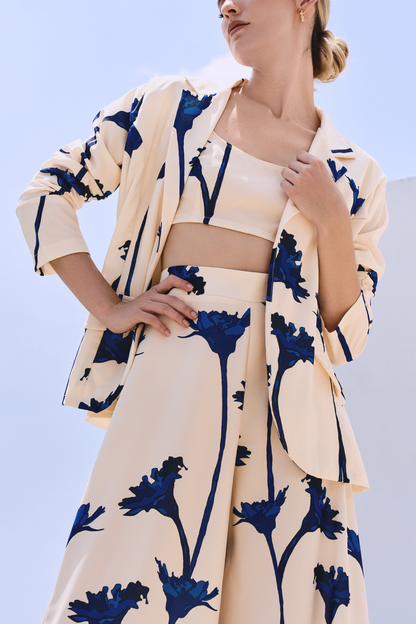 A model wearing a cream blazer and flowy pants with blue flowers by Monica Arguedas