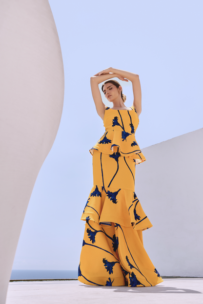 A model wearing a yellow squared-neck top with a yellow skirt with blue flowers and ruffles by Monica Arguedas