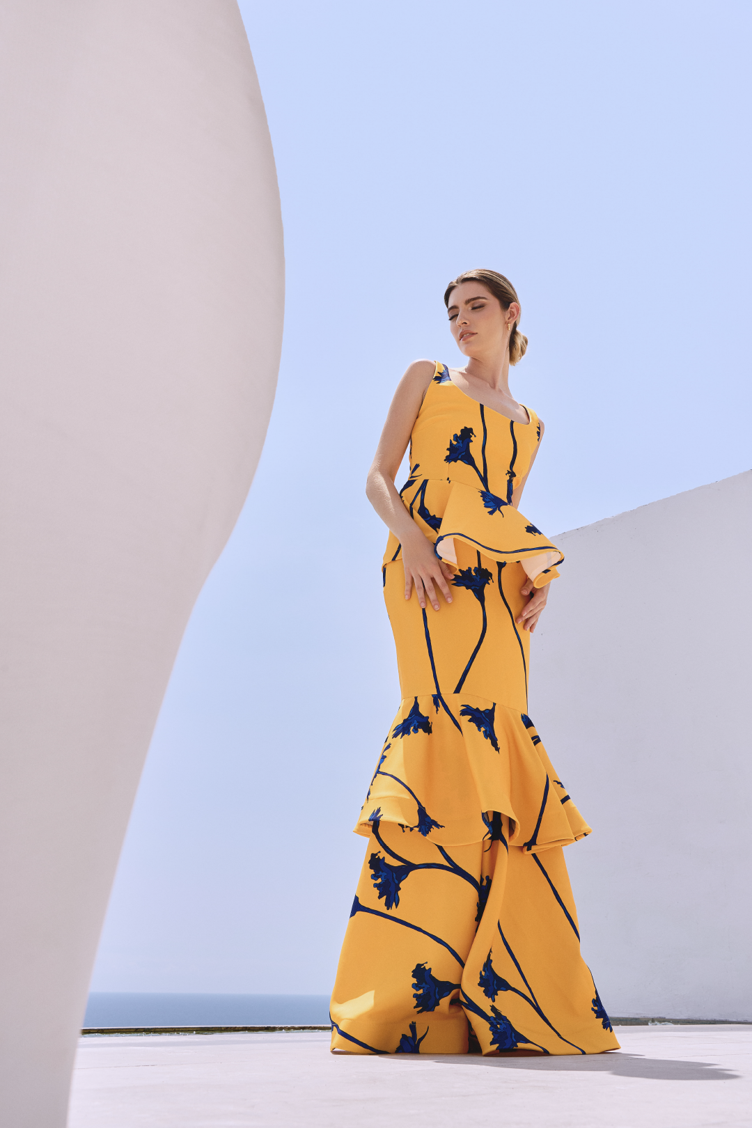 A model wearing a yellow squared-neck top with a yellow skirt with blue flowers and ruffles by Monica Arguedas