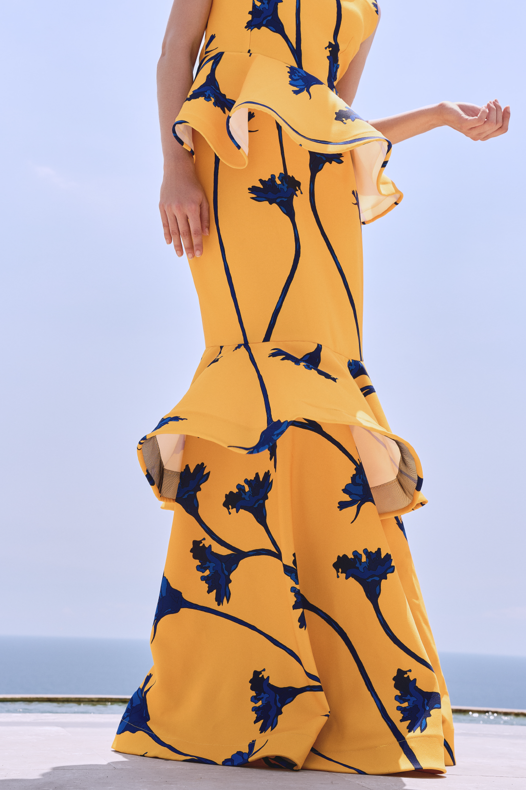 A model wearing a yellow skirt with blue flowers and ruffles by Monica Arguedas