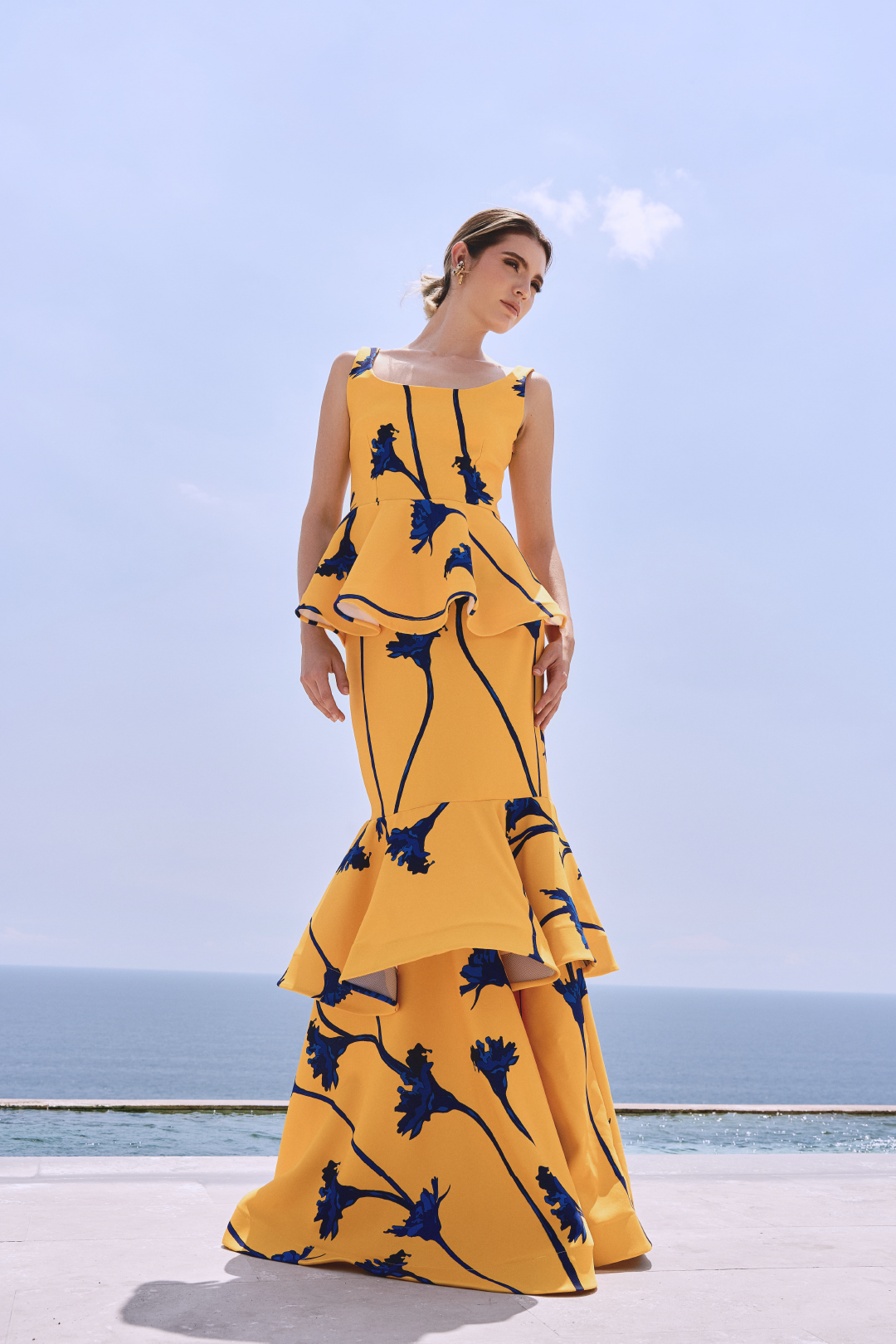 A model wearing a yellow squared-neck top with a yellow skirt with blue flowers and ruffles by Monica Arguedas