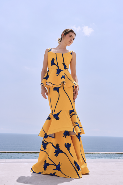 A model wearing a yellow squared-neck top with a yellow skirt with blue flowers and ruffles by Monica Arguedas
