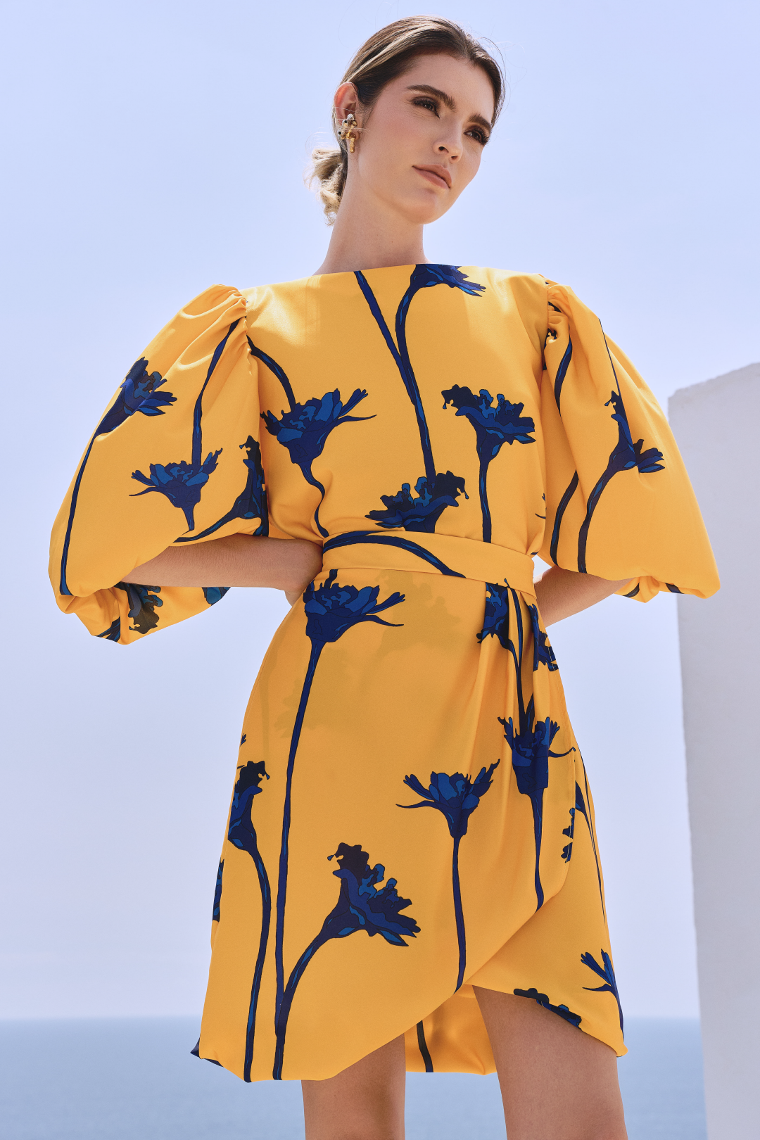 A model wearing a yellow top with blue flowers and a bow detail on the back; and a yellow skirt with blue flowers by Monica Arguedas
