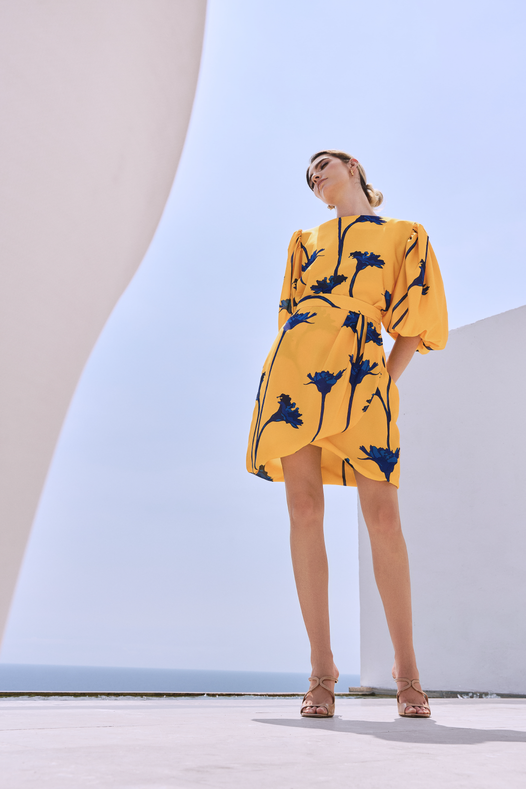 A model wearing a knee-length yellow skirt with blue flowers by Monica Arguedas
