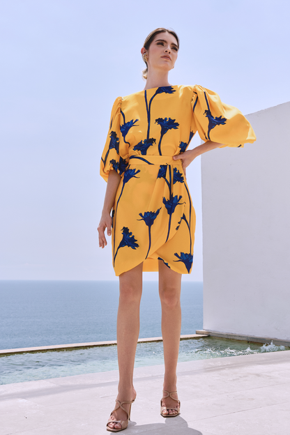 A model wearing a knee-length yellow skirt with blue flowers by Monica Arguedas