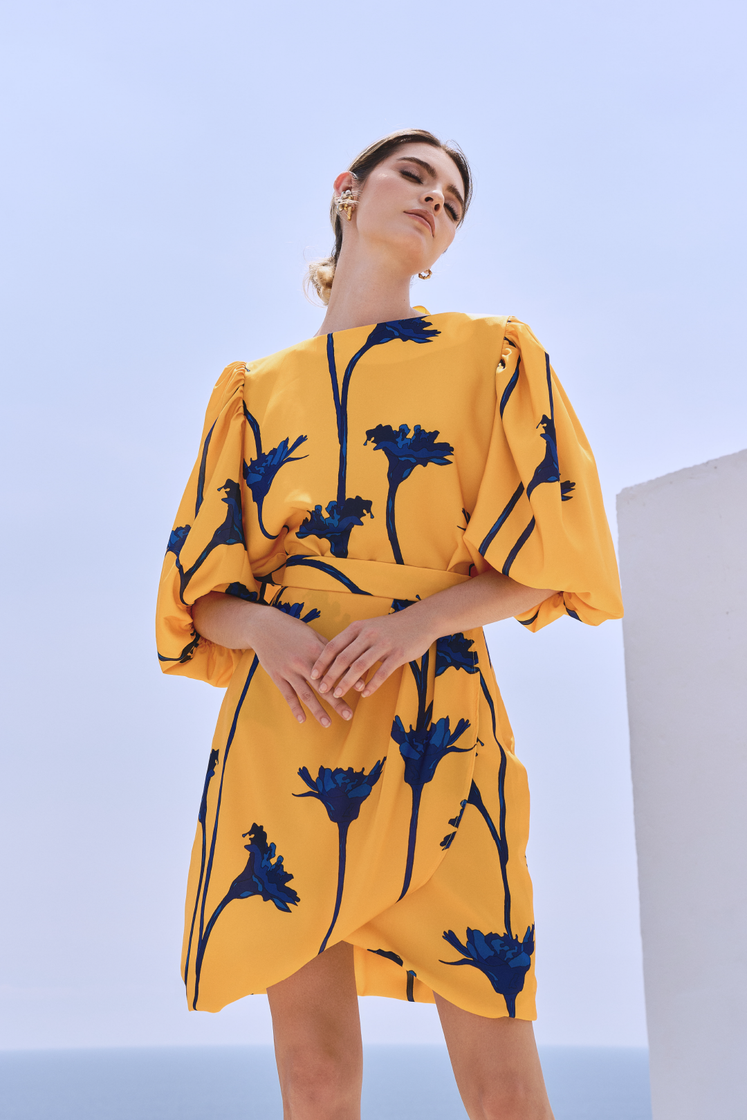 A model wearing a yellow top with blue flowers and a bow detail on the back by Monica Arguedas